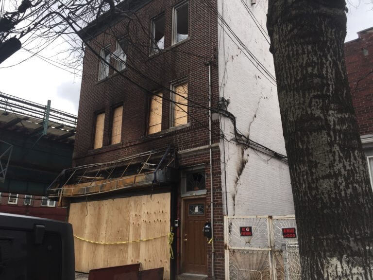 Exterior view of damaged apartment building. View of boarded up building