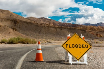traffic cones and road sign with the words "Flooded", located on the side of road.