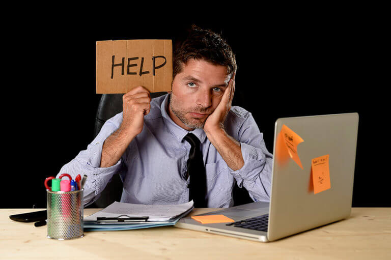 View of man at desk holding up "Help" sign made of carboard