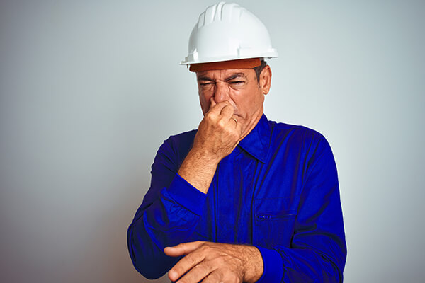 Handsome middle age worker man wearing uniform and helmet over isolated white background smelling something stinky and disgusting, intolerable smell, holding breath with fingers on nose. Bad smells concept.